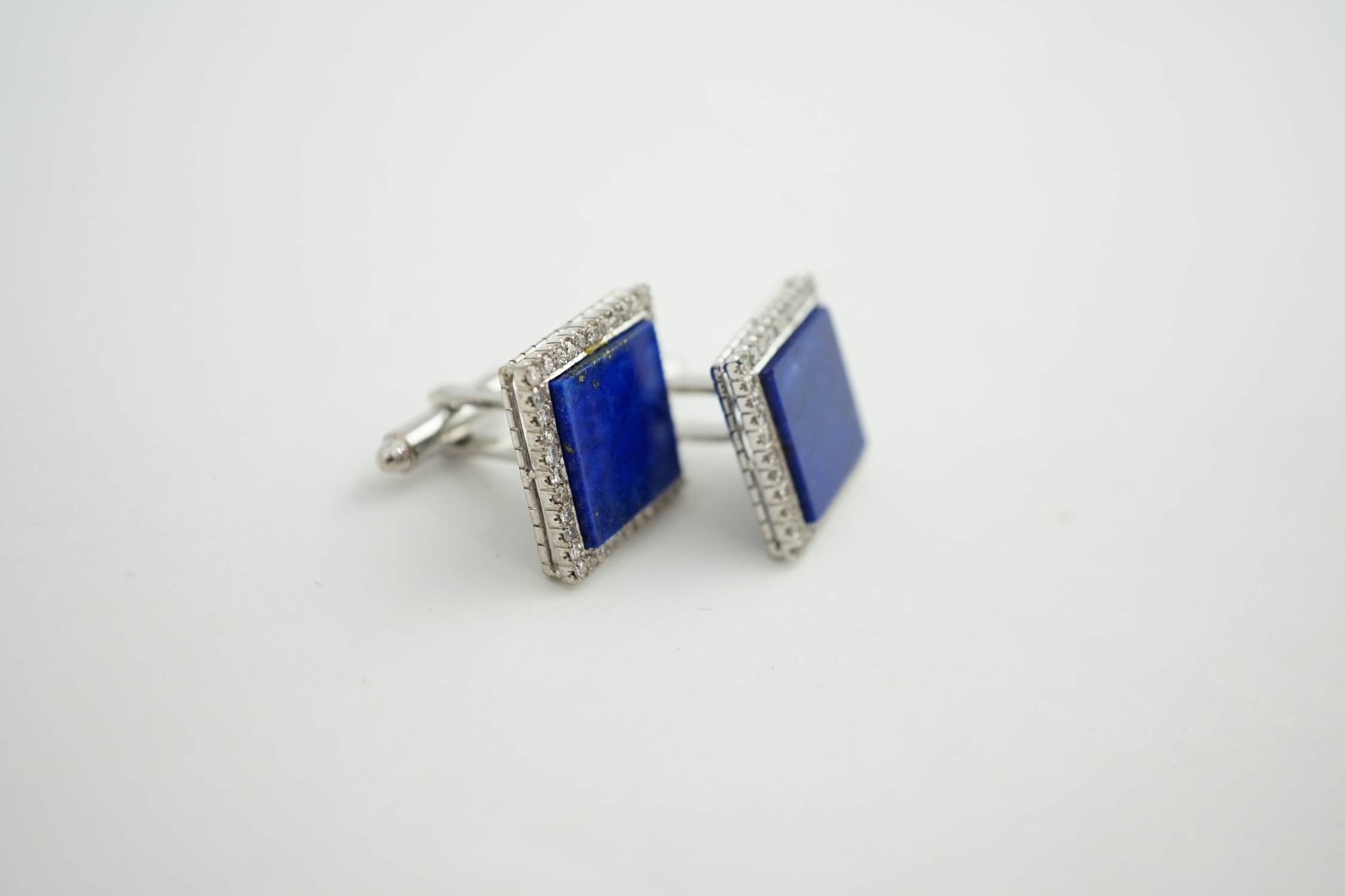 A pair of 18K white metal, lapis lazuli and diamond set tablet cufflinks, each lapis stone surrounded by forty claw set diamonds, 17mm, gross weight 14.1 grams. Condition - fair